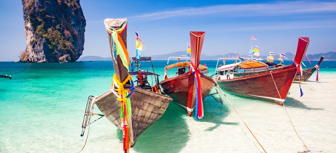 Longtail-Boote am Strand von Poda Island bei Krabi in Thailand mit türkisblauem Meer und Kalksteinfelsen.