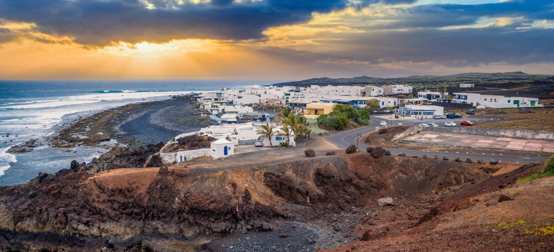 Blick auf das Fischerdorf El Golfo auf Lanzarote mit weißen Häusern, schwarzer Lavaküste und Sonnenuntergang über dem Atlantik.