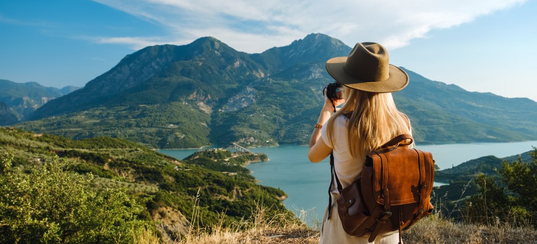 Frau mit großem Rucksack macht Fotos von Bergen und blauem See.
