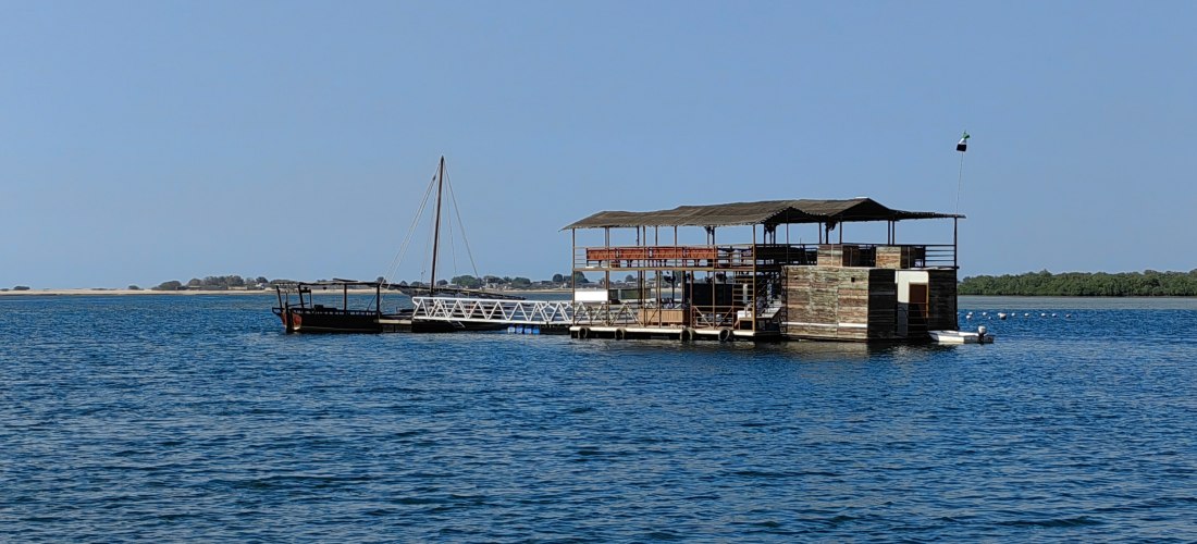 Schwimmendes Ponton der Suwaidi Pearl Farm in Ras Al Khaimah mit traditionellem Holzboot und Mangroven im Hintergrund.