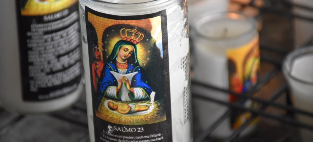 Nahaufnahme einer Votivkerze mit dem Bildnis der Jungfrau Maria mit Krone, die ein Gebet hält, darunter ein schlafendes Jesuskind. Auf der Kerze ist auch Psalm 23 in spanischer Sprache abgedruckt