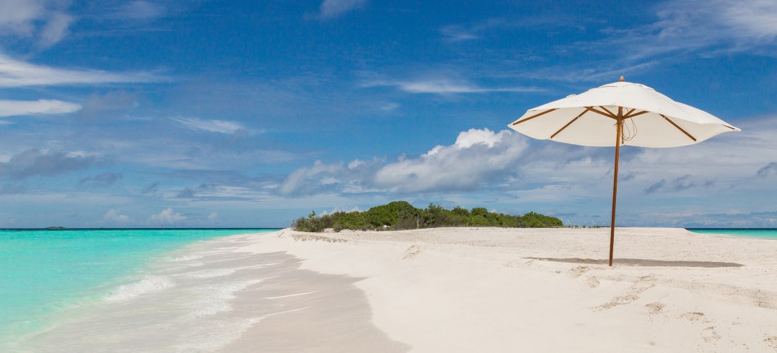 Idyllischer Strand auf den Malediven mit weißem Sonnenschirm, feinem Sand und kristallklarem Wasser.