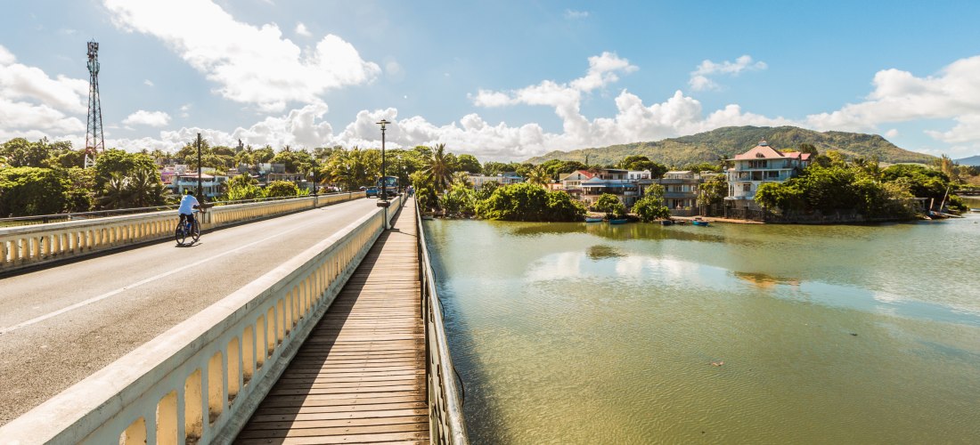 Brücke über den Fluss in Mahébourg mit Blick auf Kolonialhäuser, Palmen und die umliegenden Berge auf Mauritius