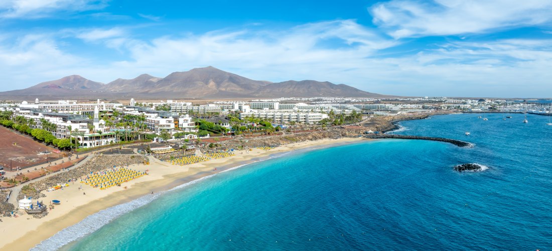 Panoramablick auf Playa Blanca auf Lanzarote mit Sandstrand, türkisblauem Meer, Hotelanlagen und Yachthafen.