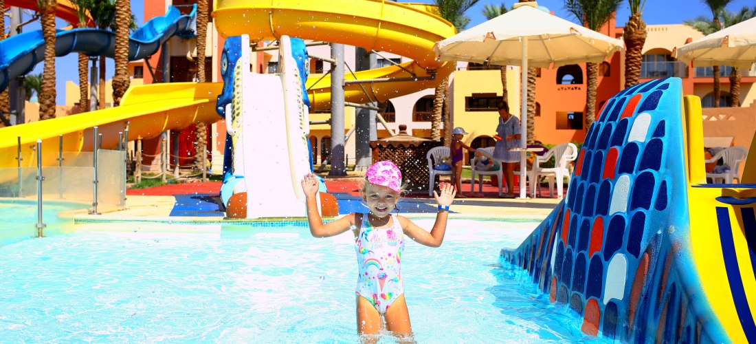 Ein Mädchen in Badeanzug und rosa Mütze spielt an einem heißen, sonnigen Tag in einem Badehaus. Schwimmen für Kinder. Ausgezeichnete Bedingungen für einen Familienurlaub. Aktive Erholung am Meer.