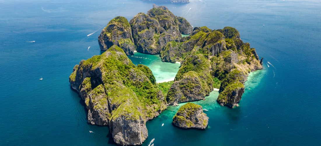 Die Aufnahme zeigt eine spektakuläre Luftansicht der Phi-Phi-Inselgruppe in der Provinz Krabi, Thailand. Zu sehen sind grün bewachsene Kalksteinfelsen, die steil aus dem azurblauen Meer emporragen. Dazwischen befinden sich mehrere kleine Buchten mit feine