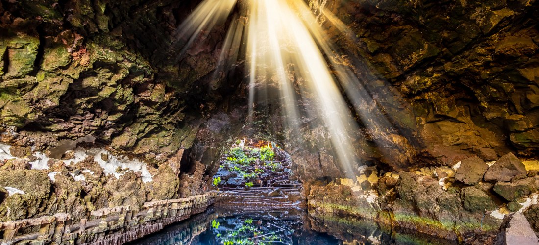 Lichtstrahlen fallen in die Lavahöhle Jameos del Agua auf Lanzarote und spiegeln sich im Wasser.