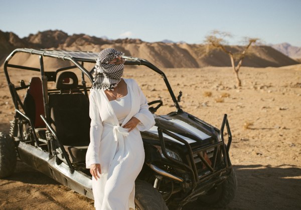 Frau vor einem Buggy in der Wüste, im Hintergrund sind Berge