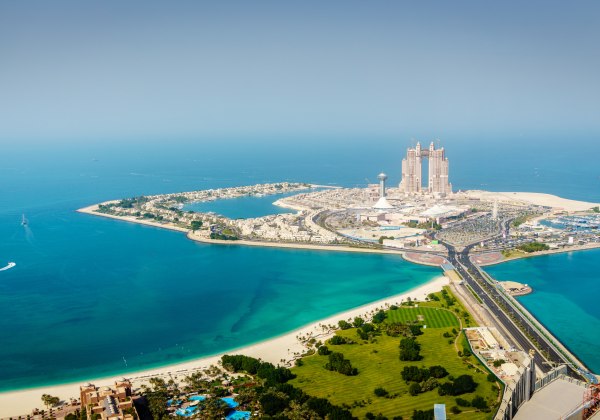 Luftaufnahme der Insel Abu Dhabi mit türkisfarbenem Wasser, modernen Hochhäusern und einer Brücke, die die Insel mit dem Festland verbindet