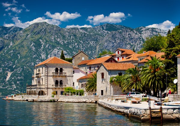Mittelmeer-Küstenstadt mit traditionellen Steinhäusern und roten Ziegeldächern vor grünen Bergen in Montenegro