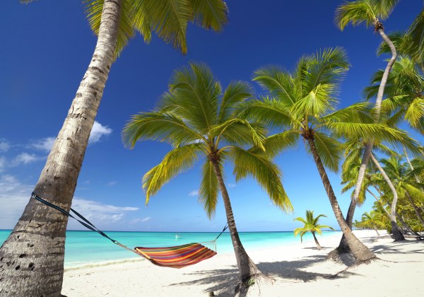 Bunte Hängematte zwischen Palmen an einem tropischen Sandstrand mit türkisfarbenem Meer und strahlend blauem Himmel