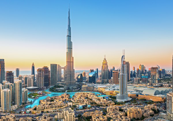 Panorama der Skyline von Dubai bei Sonnenuntergang mit dem Burj Khalifa im Zentrum. Zahlreiche moderne Hochhäuser und Wasserflächen prägen das Stadtbild.