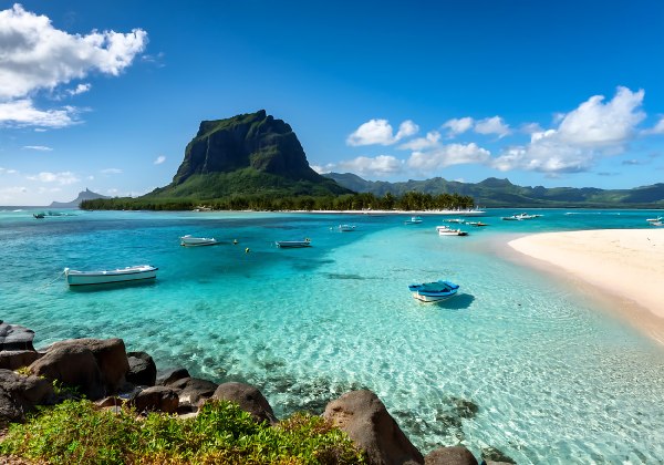 türkisfarbenes Wasser am Strand, Boote und Berge im Hintergrund