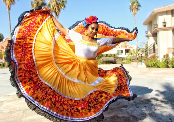 Mexikanische Tänzerin in einem bunten, traditionellen Kleid mit gelben und roten Farbtönen führt einen folkloristischen Tanz auf, während sie das Kleid schwungvoll bewegt