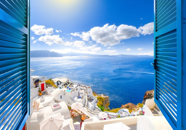 Blick durch ein offenes Fenster mit blauen Fensterläden auf die Caldera, das Meer und das weiße Dorf Oia auf der Insel Santorin, Griechenland