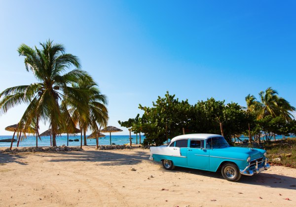 Klassischer Oldtimer in Blau-Weiß unter Palmen an einem karibischen Strand
