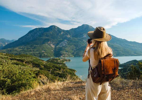 Frau mit großem Rucksack macht Fotos von Bergen und blauem See.