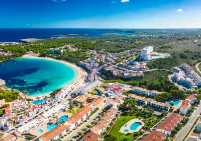 Menorca: Küstenbucht mit Strand und Ortschaft aus der Vogelperspektive