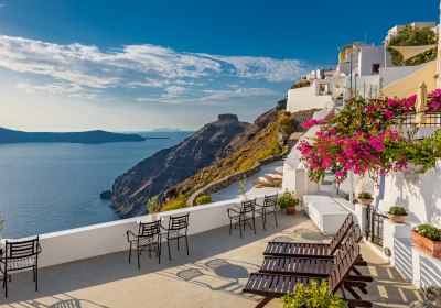 Weiße Häuser am Hang und Terrasse mit Blick auf Meer und Felsenküste in Griechenland