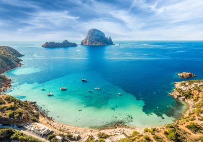 Küstenbucht auf Ibiza mit Strand, Booten und vorgelagerter Felseninsel