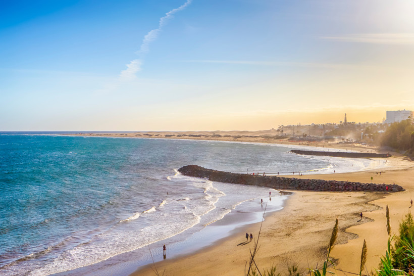 Küstenansicht von Playa del Inglés mit Sandstrand, Wellen und vorgelagertem Wellenbrecher