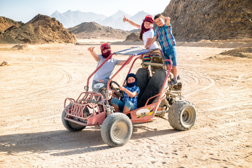 Gruppe von Kindern auf einem Buggy während einer Wüstentour zwischen Felsen und Sanddünen