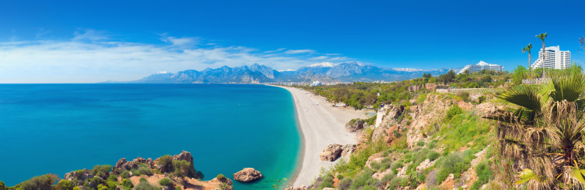 Antalya Küstenpanorama – Konyaalti Beach mit Meerblick und Taurusgebirge Panoramablick auf den Konyaalti Beach in Antalya mit kristallklarem Meer, Kiesstrand, grüner Küstenlandschaft und dem beeindruckenden Taurusgebirge im Hintergrund.