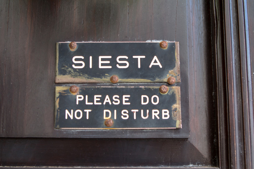 Türschild mit der Aufschrift „Siesta“ und „Please do not disturb“ an einer dunklen Holztür