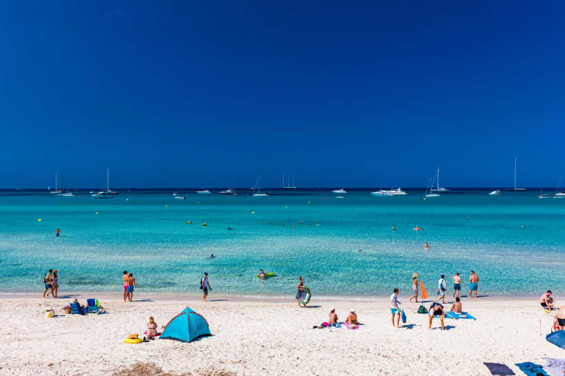 Strand Es Trenc mit Badegästen im flachen, türkisfarbenen Meer und Booten am Horizont