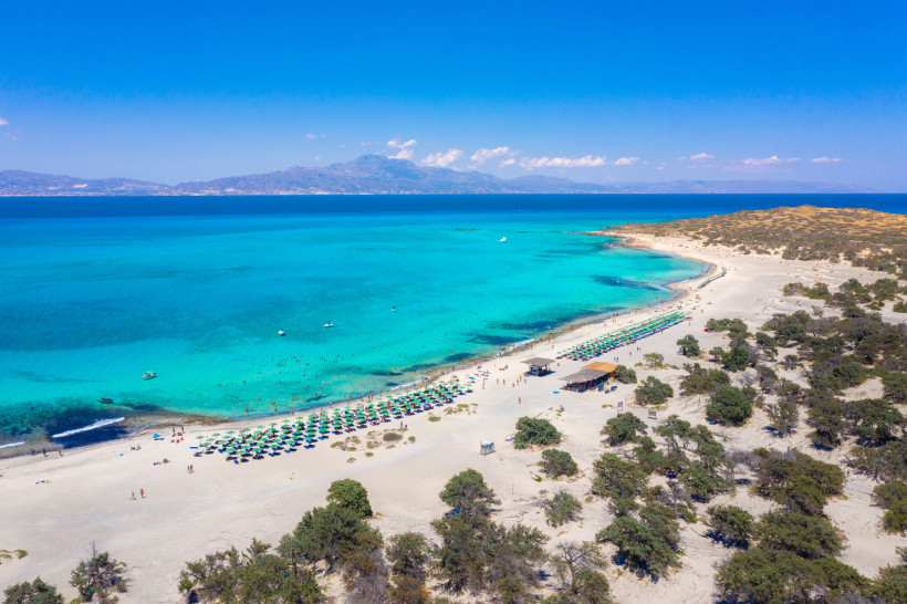 Luftaufnahme der Insel Chrissi mit Sandstrand, türkisfarbenem Meer und Sonnenschirmen