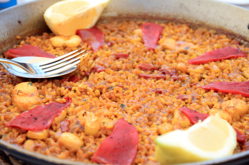 Arroz a banda in der Pfanne mit Garnelen, Paprika und Zitrone Arroz a banda in einer Pfanne, Reisgericht mit Garnelen, roten Paprikastreifen und Zitronenspalten