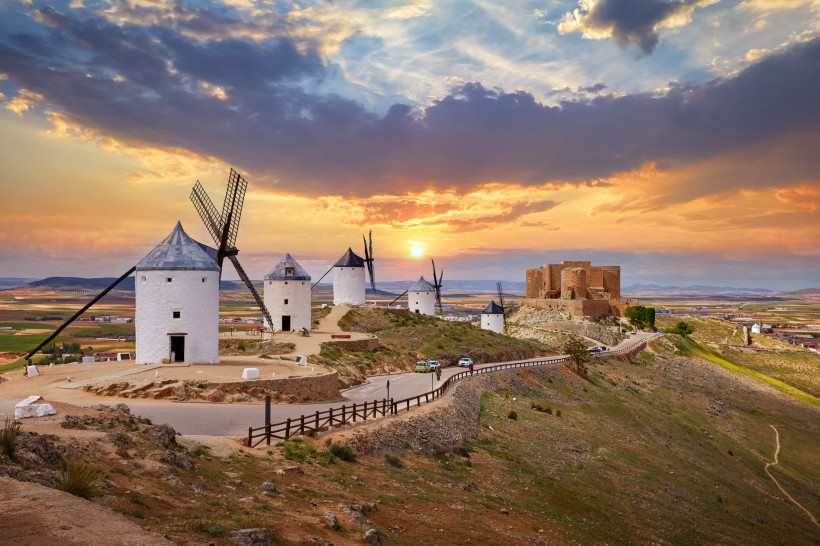 Windmühlen von Consuegra auf einem Hügel bei Sonnenuntergang, mit Burg im Hintergrund
