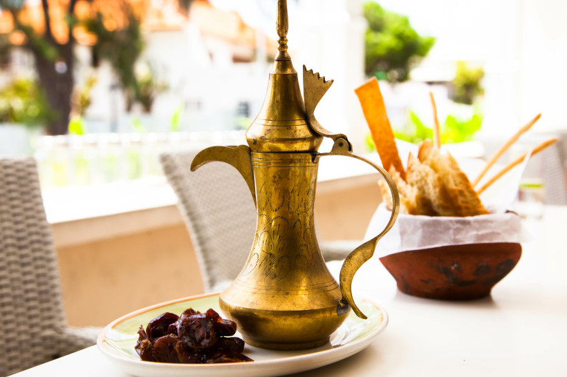 Ramadan, Kaffekanne aus gold auf einem Tisch, mit Datteln und Marshmallows, Brot im Hintergrund.