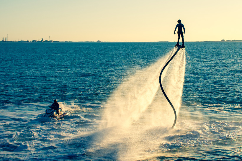 Ras al Khaimah, Aktivurlaub  Person schwebt auf einem Flyboard über dem Meer, angetrieben von Wasserstrahlen, mit Jet-Ski im Hintergrund
