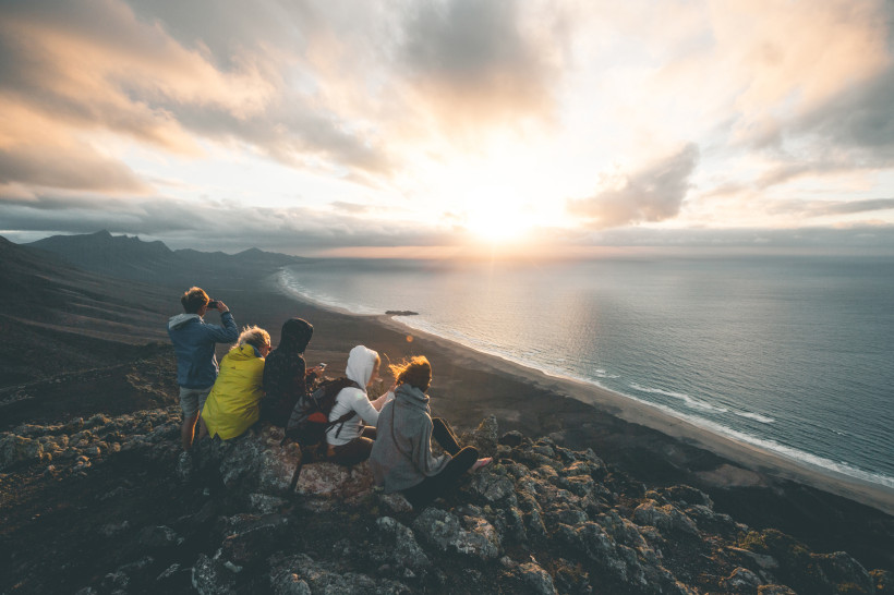 Fuerteventura – Sonnenuntergang mit Freunden über der Westküste Gruppe von Reisenden beobachtet den Sonnenuntergang über der Küste von Fuerteventura