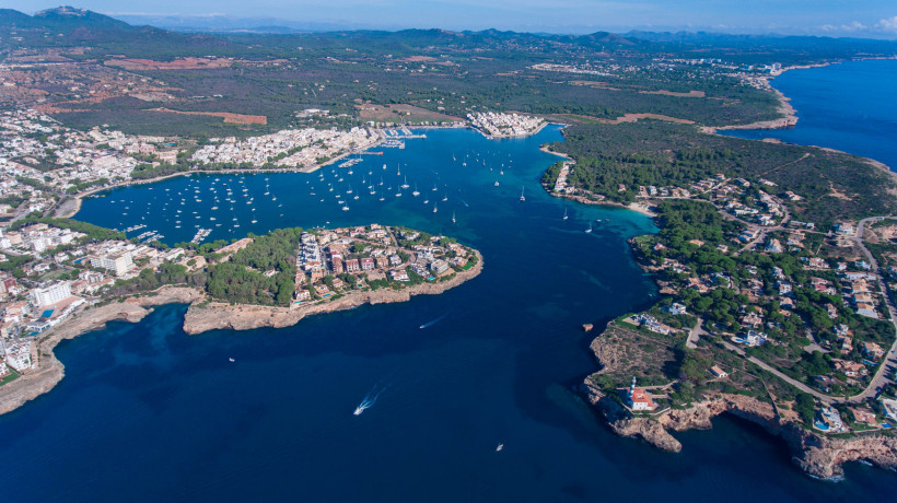 Luftaufnahme der Bucht von Portocolom mit Segelbooten, Küstenbebauung und umliegenden Pinienwäldern