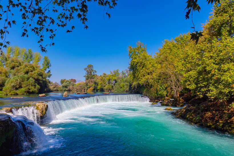 Manavgat-Wasserfall mit türkisfarbenem Wasser und dichter Vegetation am Flussufer