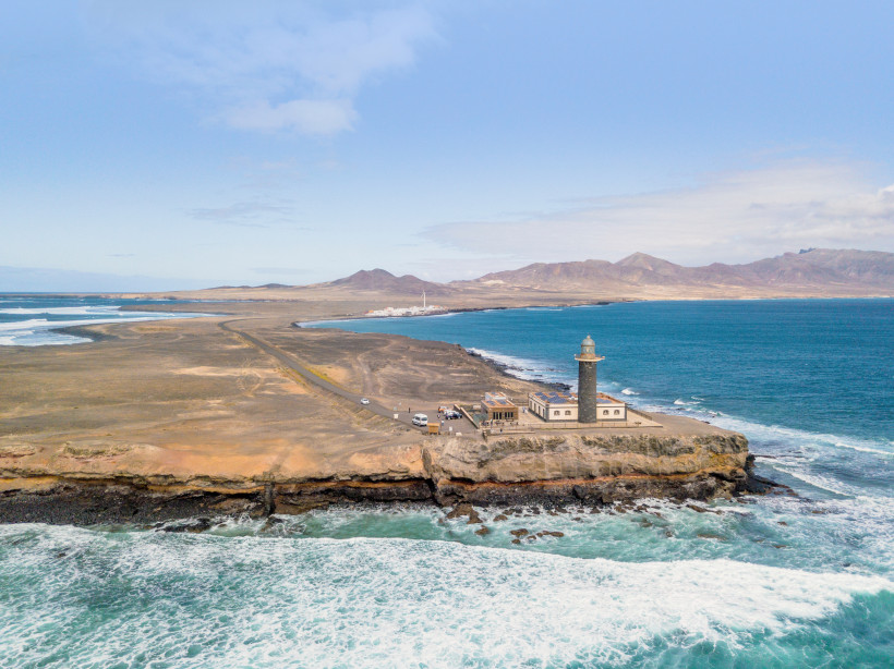 Leuchtturm an der Punta de Jandía auf Fuerteventura, Küstenlandschaft mit Meer und Bergen im Hintergrund