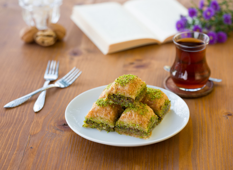 Türkische Baklava mit Pistazien und ein Glas Tee auf einem Holztisch – traditionelle Süßspeise in Kemer