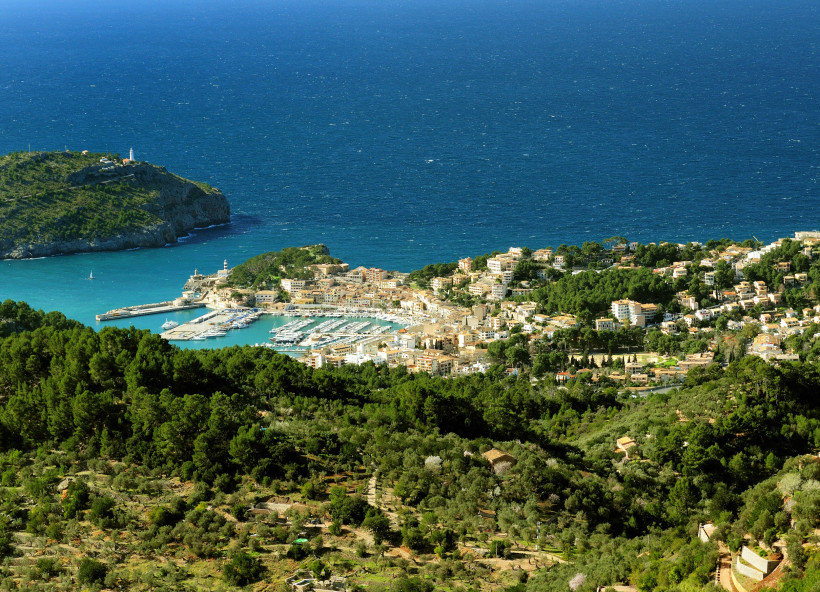 Mallorca - Mirador de Ses Barques Die Bilderserie zeigt eine malerische Küstenstadt am Mittelmeer, die von einer üppigen, grünen Landschaft mit Olivenhainen und Pinienwäldern umgeben ist. Im Vordergrund sind sanfte Hügel und grüne Bäume zu sehen, dahinter erstreckt sich die Küste mit eine