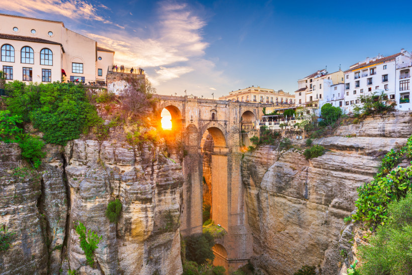 Die Puente Nuevo in Ronda bei Sonnenuntergang. Die beeindruckende Steinbrücke überspannt eine tiefe Schlucht und verbindet die Altstadt mit dem neueren Stadtteil. Sonnenlicht scheint durch den mittleren Brückenbogen.