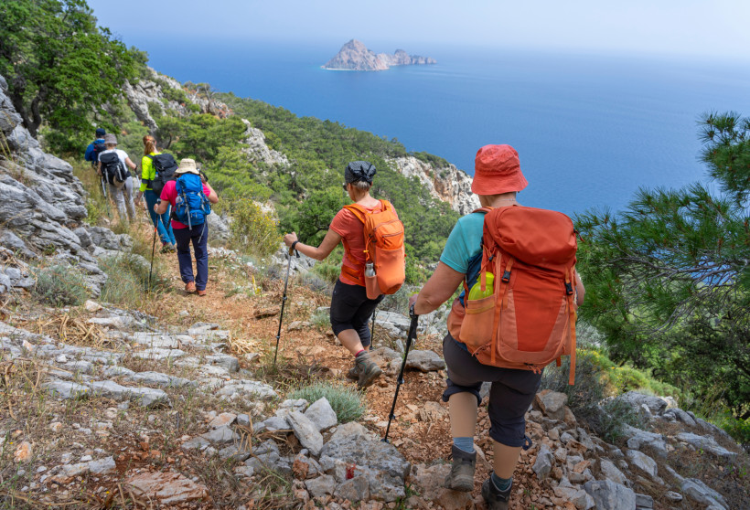 Entlang schmaler Pfade und steiler Felsen führt diese Wanderung durch die atemberaubende Küstenlandschaft der Türkischen Riviera. Eine Gruppe Wandernder genießt den Weitblick über das azurblaue Mittelmeer, mit einer kleinen Insel am Horizont. Natur, Beweg