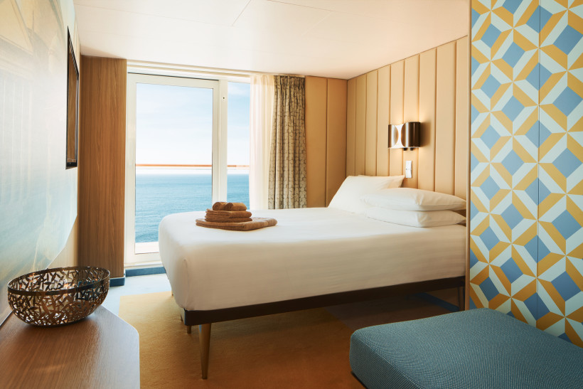 Balkonkabine auf der Costa Smeralda mit Doppelbett und Blick aufs Meer durch die Balkontür
