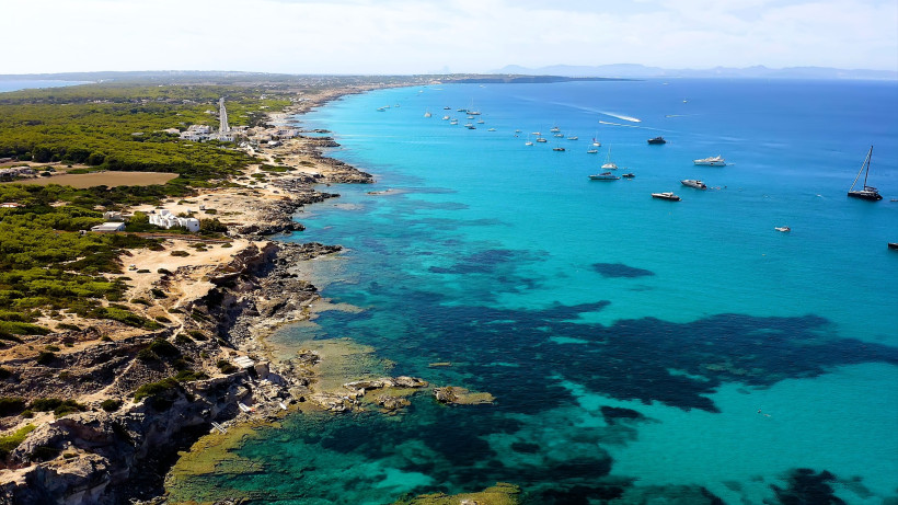 Luftaufnahme der Küste von Formentera mit türkisblauem Meer, Felsenstrand und vor Anker liegenden Booten
