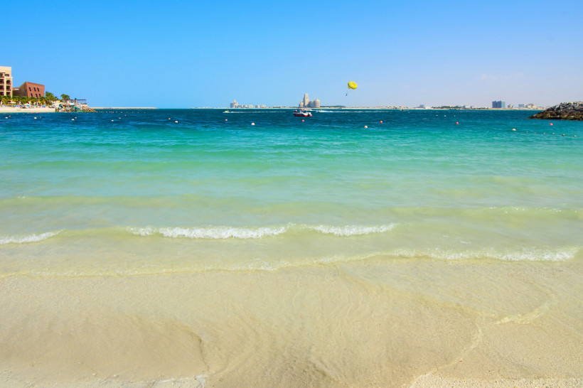 Strand von Ras Al Khaimah mit türkisblauem Meer, Parasailing und Blick auf Hotels – beliebtes Reiseziel in den Vereinigten Arabischen Emiraten.