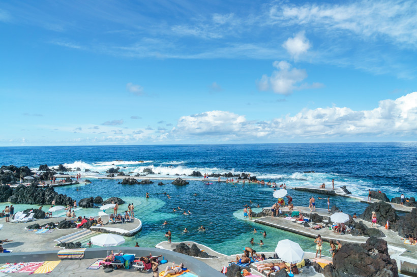 Natürliche Lavapools in Porto Moniz auf Madeira mit Badegästen und Blick auf den Atlantik unter blauem Himmel