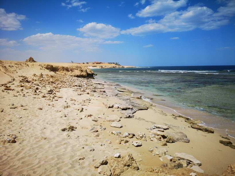 Natürlicher, ruhiger Strand mit Felsen und türkisfarbenem Wasser Unberührter, felsiger Sandstrand mit klarem, flachem Meer und blauem Himmel