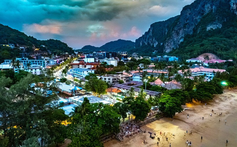 Ao Nang in Krabi bei Abenddämmerung: Lichter der Stadt, belebter Strand und Kalksteinfelsen im Hintergrund.