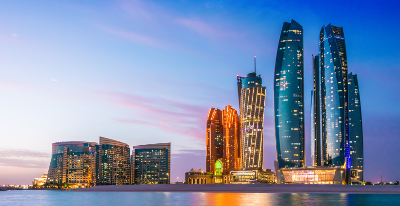 Skyline von Abu Dhabi bei Sonnenuntergang mit den beleuchteten Etihad Towers am Wasser