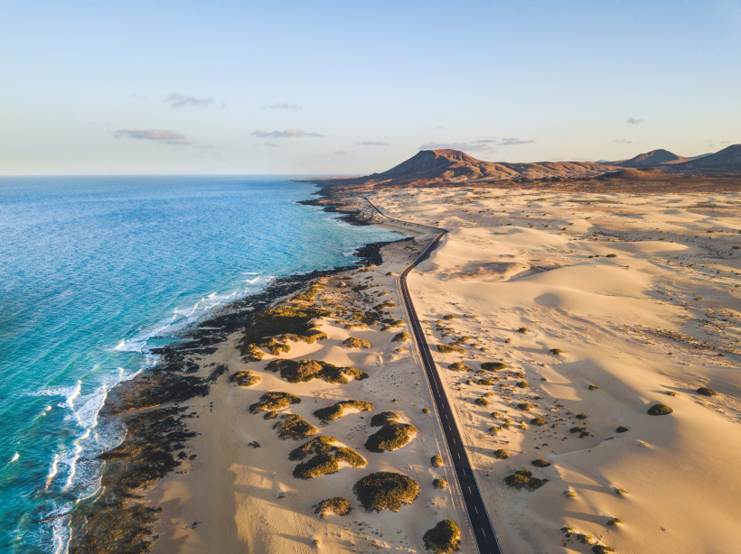 Winter auf Fuerteventura – Ruhige Strände und Sonne statt Schnee Luftaufnahme der Dünenlandschaft bei Corralejo auf Fuerteventura mit Küstenstraße und goldenem Licht – milder Winter auf den Kanaren.